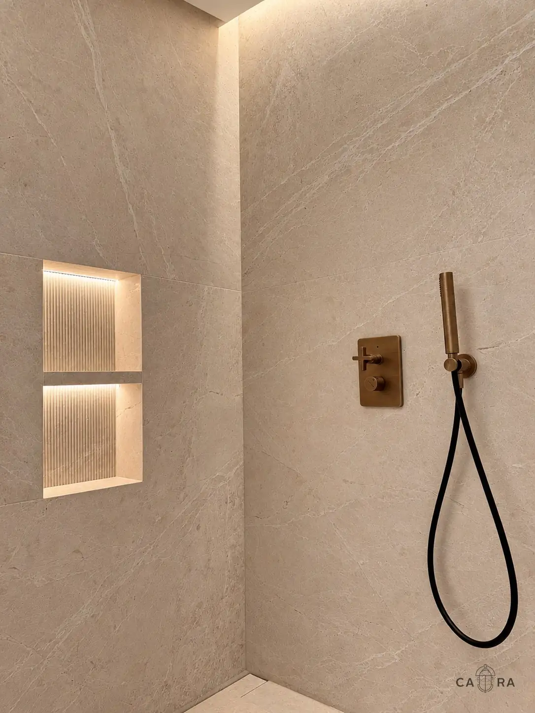 Shower in cream stone with a lit fluted niche and bronze fittings