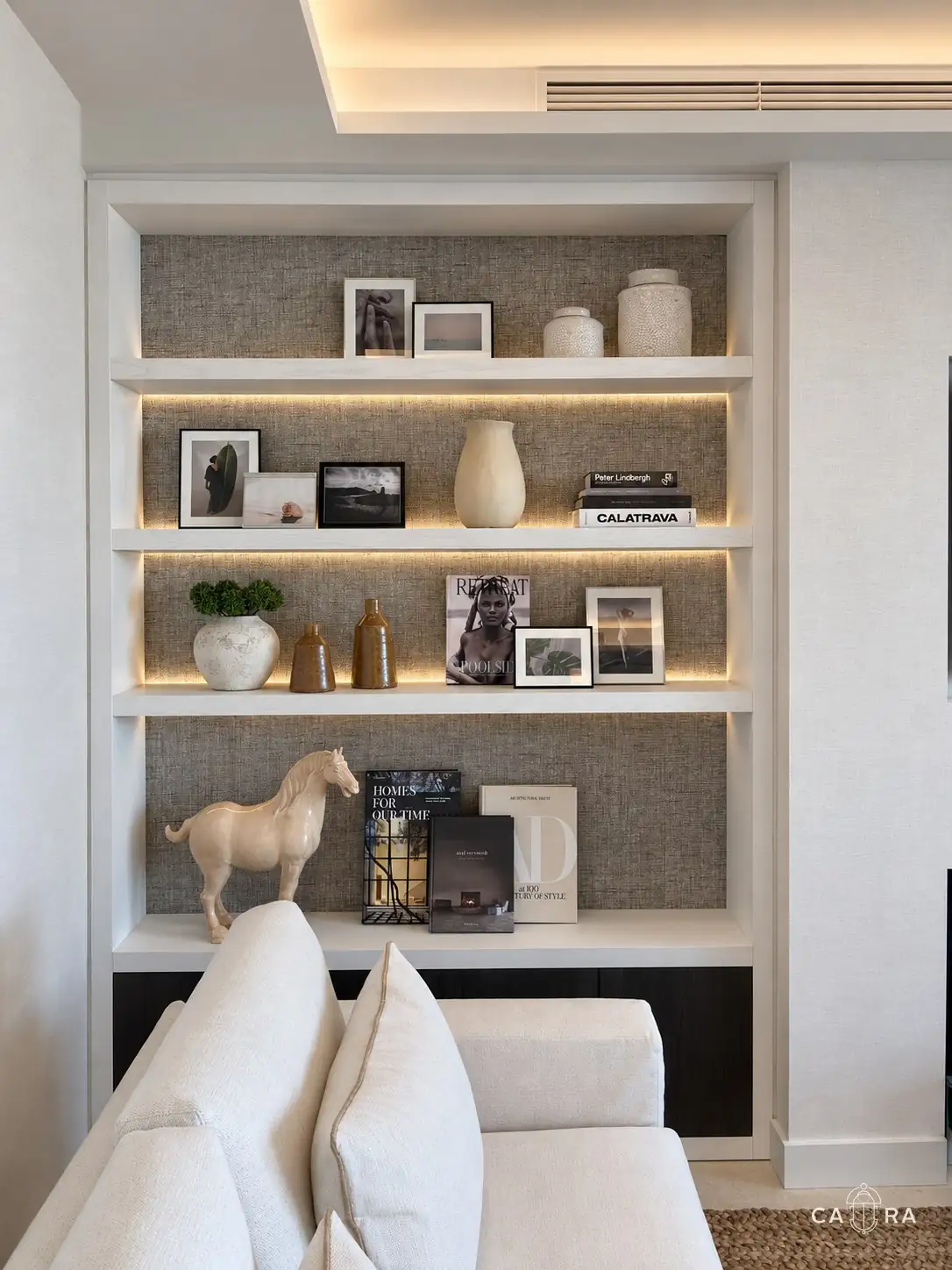 Illuminated shelving with grasscloth backing, books, ceramics and photographs
