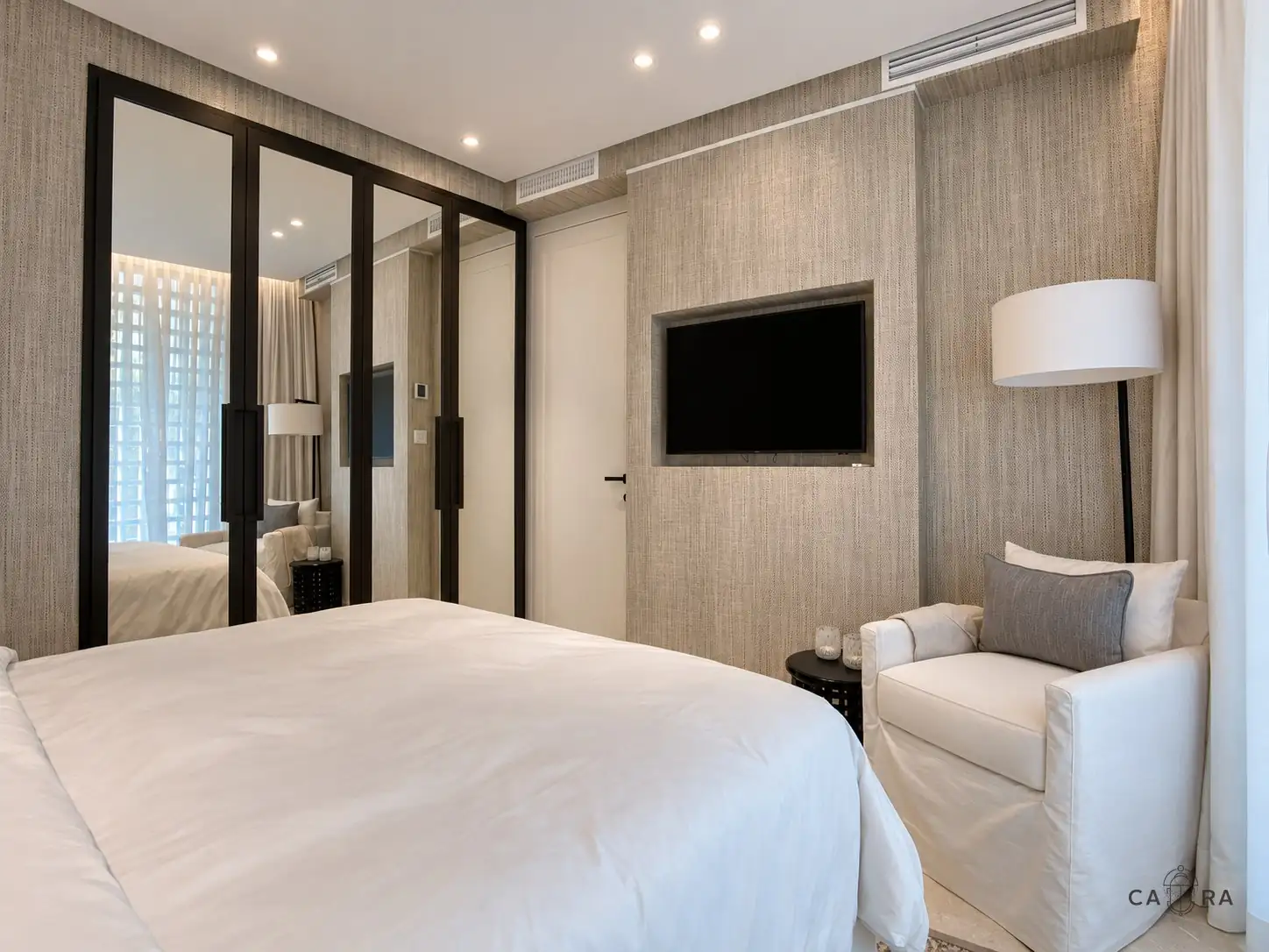 Bedroom with dark-framed mirrored wardrobe, grasscloth walls and a slipcovered armchair