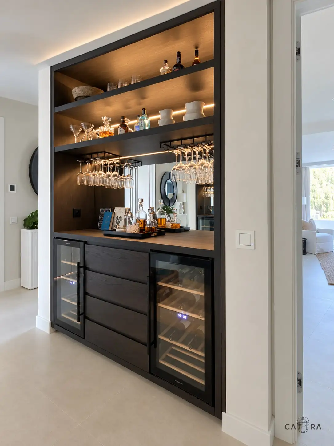 Built-in bar in dark wood with lit shelves, hanging glassware and wine fridges