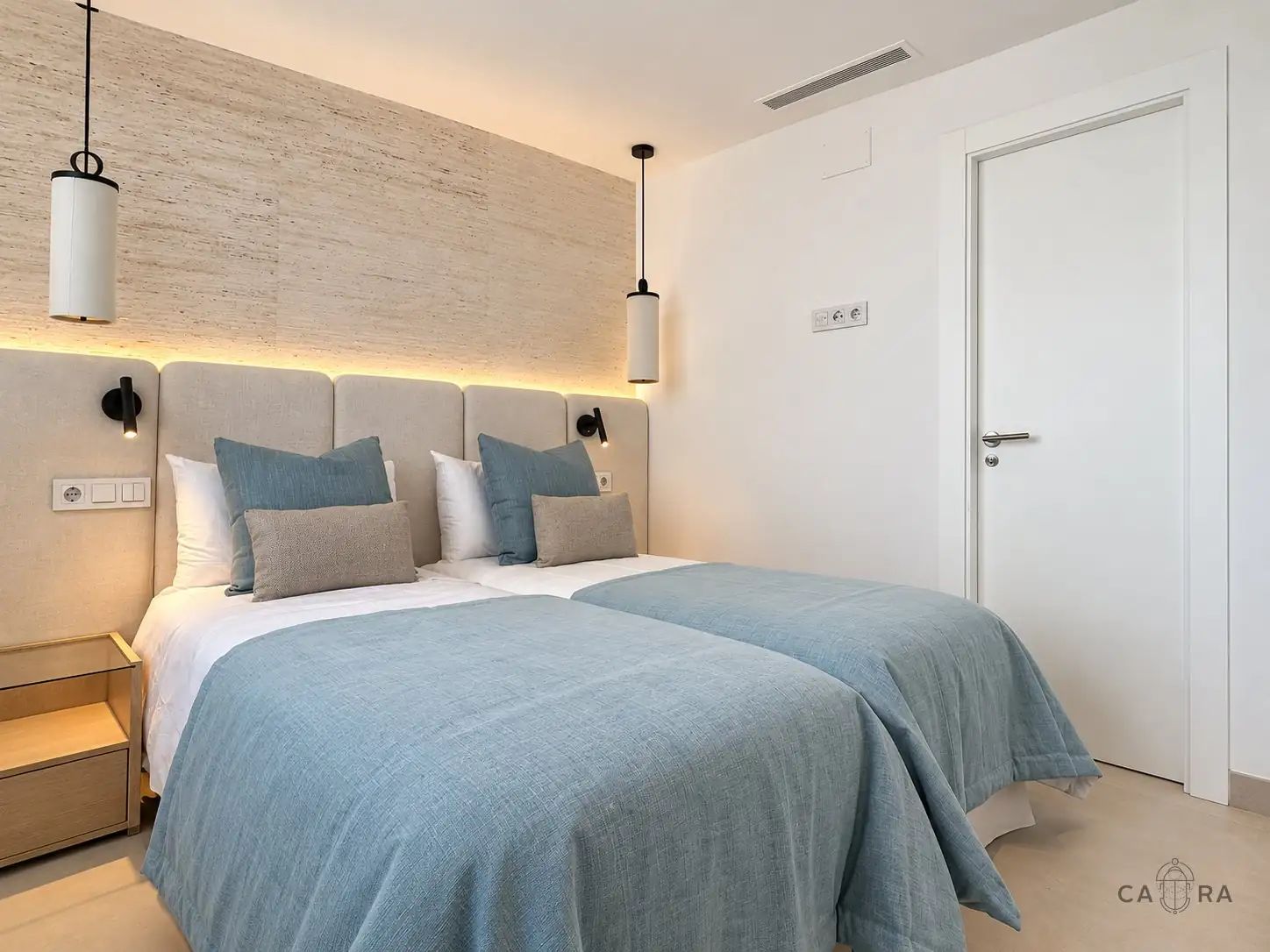 Twin bedroom with blue throws, upholstered headboards and pendant lights